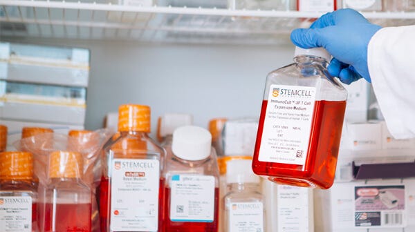 A scientist reaching for a bottle of cell culture medium from a shelf.