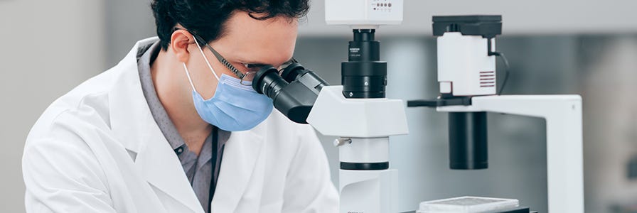 A scientist looking into a microscope while he performs the CFU assay