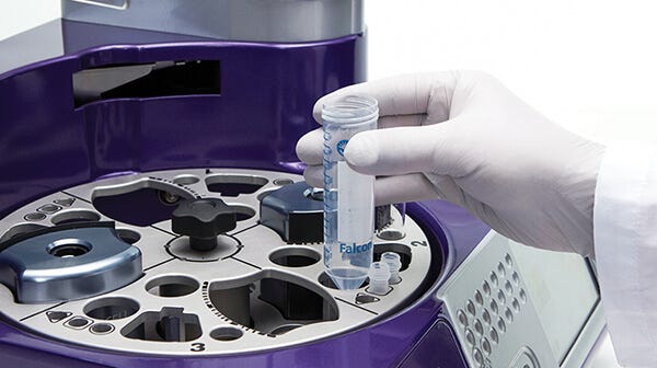 A gloved hand inserting an empty tube into a RoboSep™ instrument in preparation for automated cell isolation.